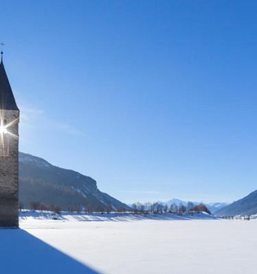 Zugefrorener Reschensee mit Kirchturm im oberen Vinschgau